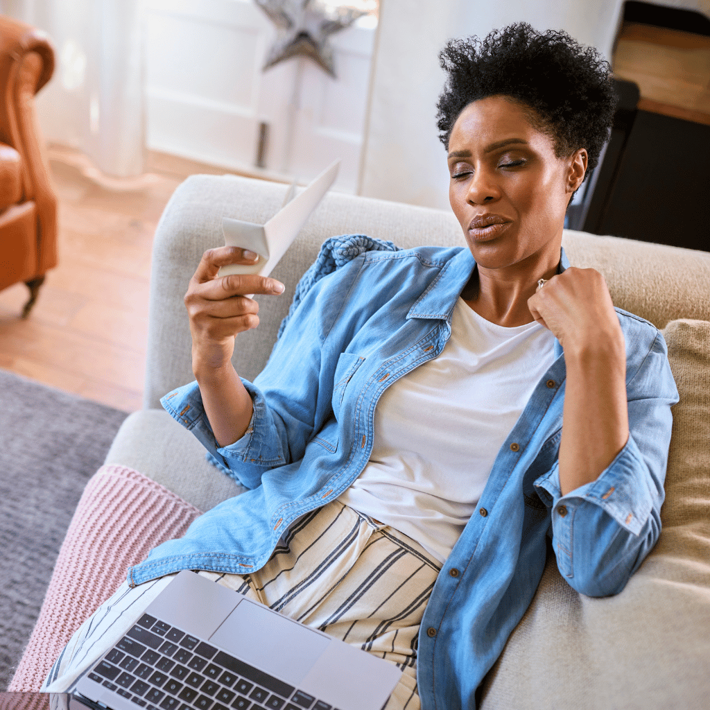Perimenopausal woman having hot flash on couch with laptop in lap, HRX